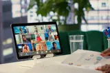 Videoconferentie op tablet met meerdere deelnemers, bureaumateriaal en kantooromgeving op de achtergrond.